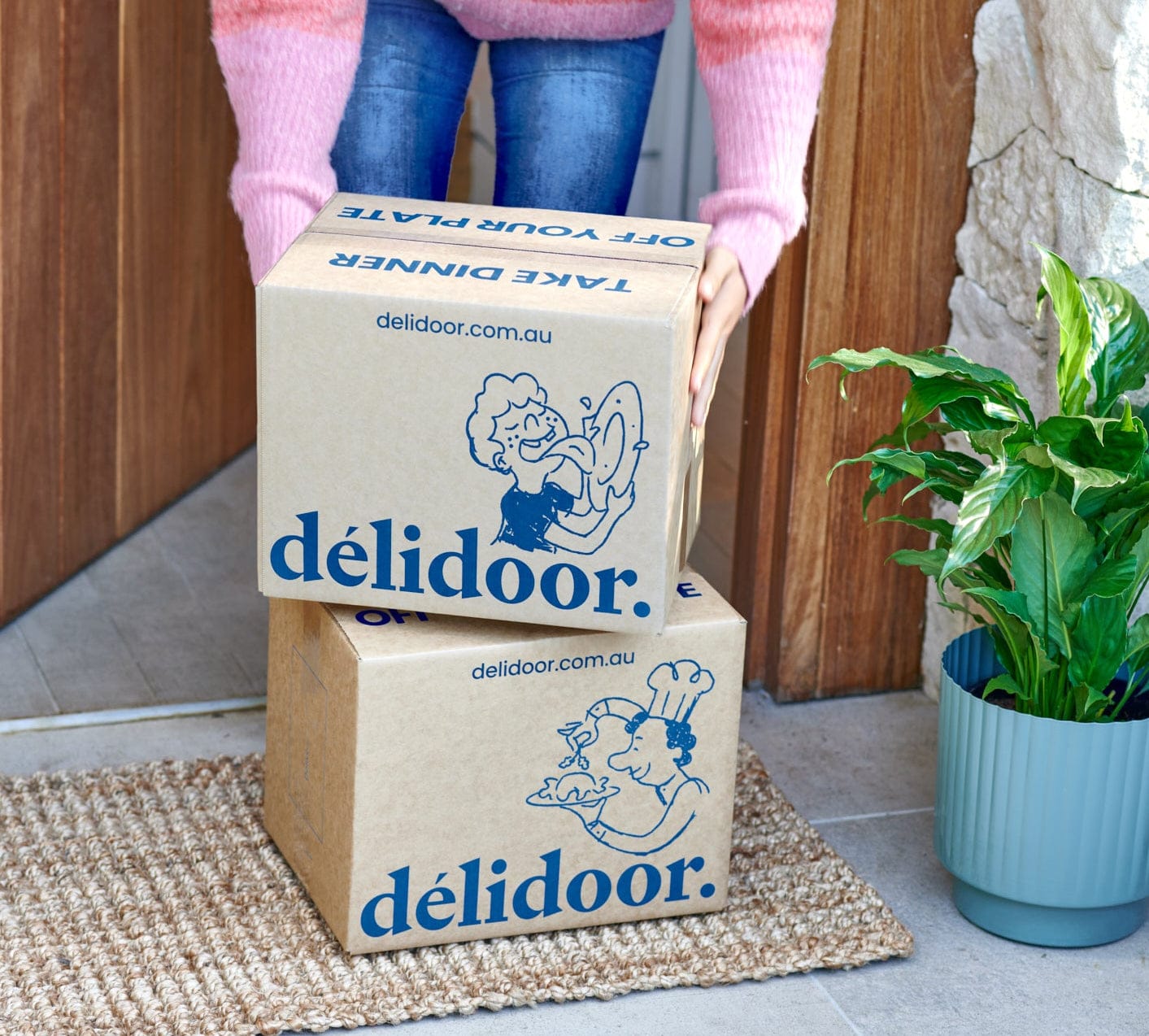 Person stacking two boxes with 'delidoor' branding on a doorstep.