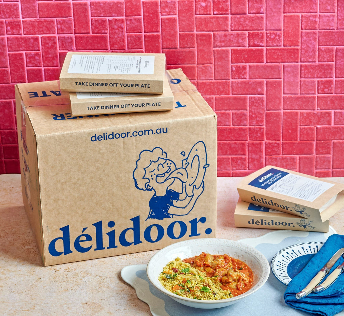 Délidoor delivery box and Meals for One trays beside a plated chicken and couscous lunch